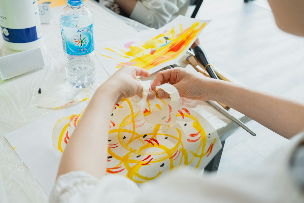 Hands working on an abstract painting with warm colours and brush strokes