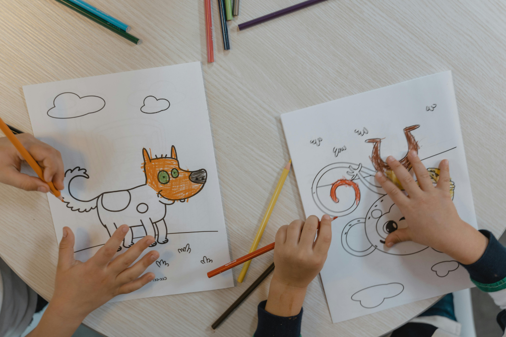 Two children colouring in cartoon animals on printed activity pages
