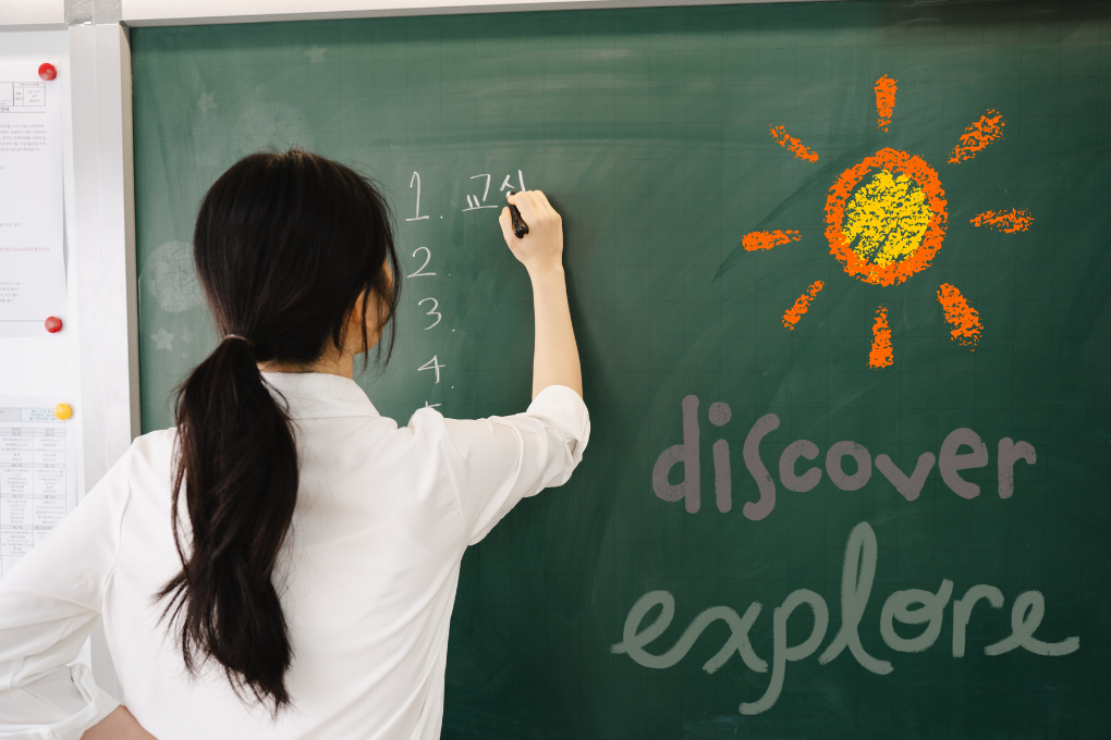 Teacher writing on chalkboard with the words “Discover” and “Explore” next to a drawn sun